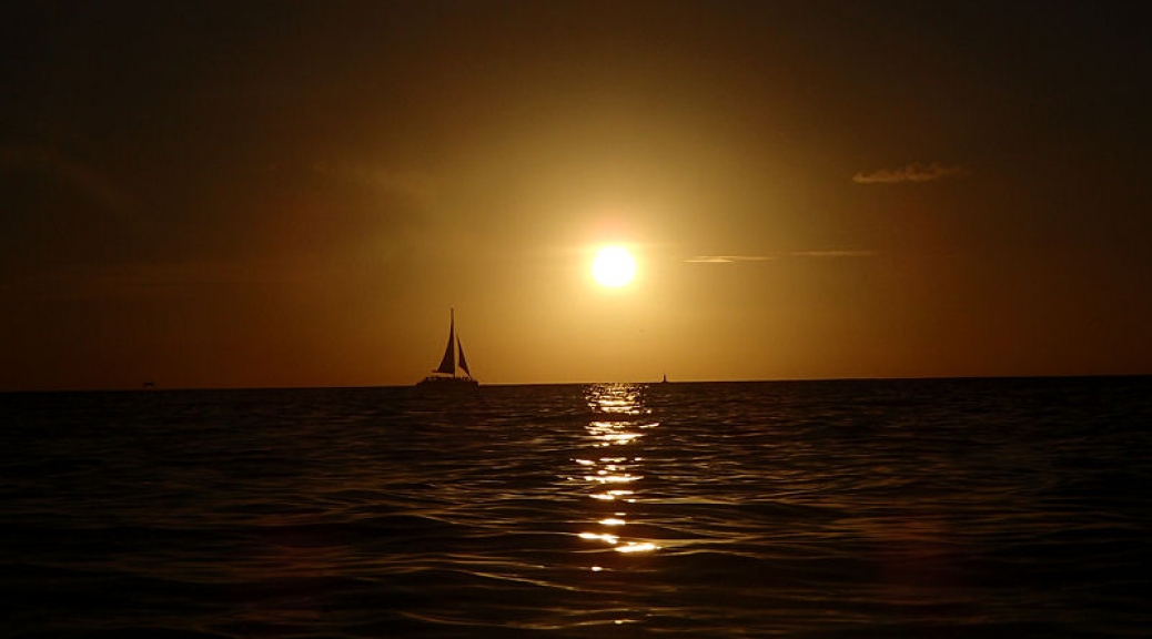 Sailboat passing the setting sun